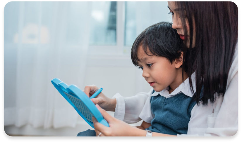 Endonezyalı bakıcı, küçük erkek çocukla birlikte oturarak mavi tablet üzerinde eğitici etkinlik yapıyor